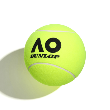 A bright yellow tennis ball with a large black 'AO' logo and the text 'DUNLOP' on it, placed on a shadowy surface.