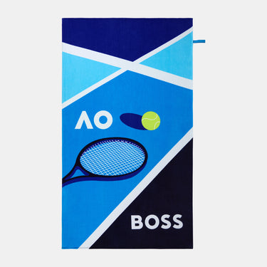 A rectangular beach towel featuring a tennis-themed design with the text 'AO' and 'BOSS', a tennis racket, a tennis ball, and geometric blue, navy, and light blue patterns on a light gray background.