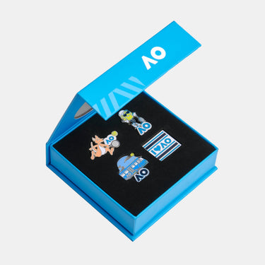 A set of four colorful enamel pins displayed inside an open bright blue presentation box with a black insert, photographed on a plain white background.