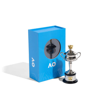 A miniature replica of women's AO trophy with a silver cup and a black base next to blue packaging against a white background. 
