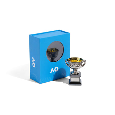 A miniature replica of men's AO trophy with a silver cup and a black base next to blue packaging against a white background. 