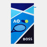 A rectangular beach towel featuring a tennis-themed design with the text 'AO' and 'BOSS', a tennis racket, a tennis ball, and geometric blue, navy, and light blue patterns on a light gray background.
