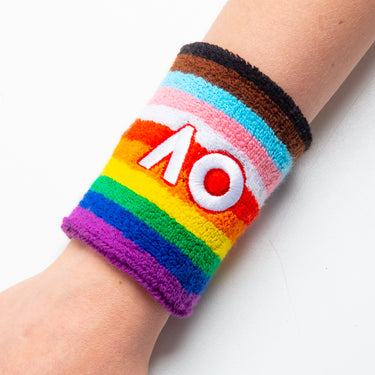 A multicolored wristband worn by a person with the AO logo on the wristband, featuring a rainbow design on a white background.
