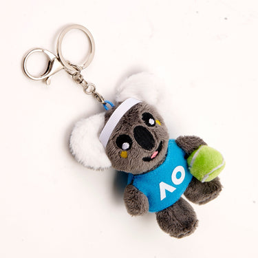 An above view of a plush koala keyring wearing a tennis hat and holding a tennis ball, with a blue badge displaying AO logo in white color.