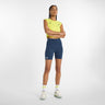 A woman wearing a yellow sports tank top and navy blue sports shorts, standing with arms crossed.