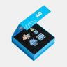 A set of four colorful enamel pins displayed inside an open bright blue presentation box with a black insert, photographed on a plain white background.