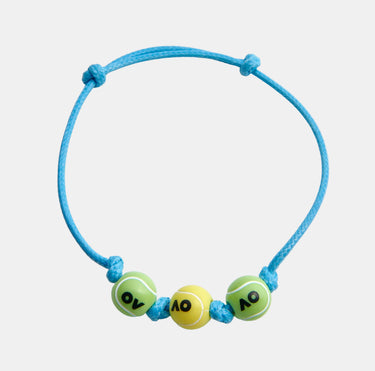 A light blue cord bracelet featuring three tennis-themed beads: two green with yellow lines and black 'AO' lettering, and one yellow with black 'AO' lettering.