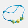 A light blue braided cord bracelet with three tennis ball charms in green, yellow, and green, featuring black lettering, on a solid white background.